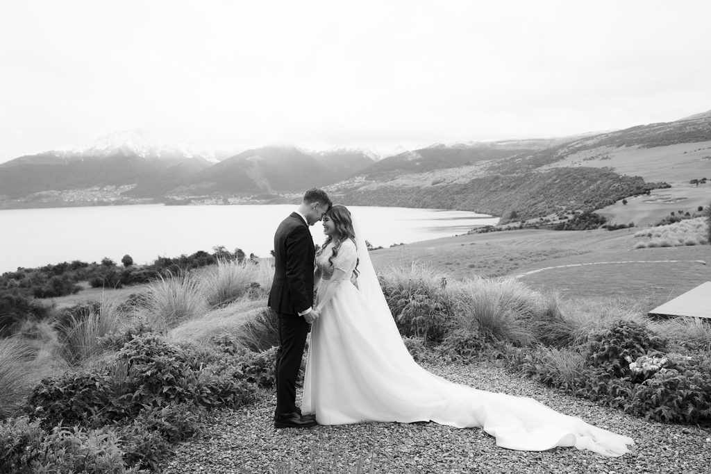 The happy bride and groom, Jaclyn and Blake, posing for photographer Kate Roberge on their rainy wedding day, overlooking Lake Wakatipu in Queenstown.